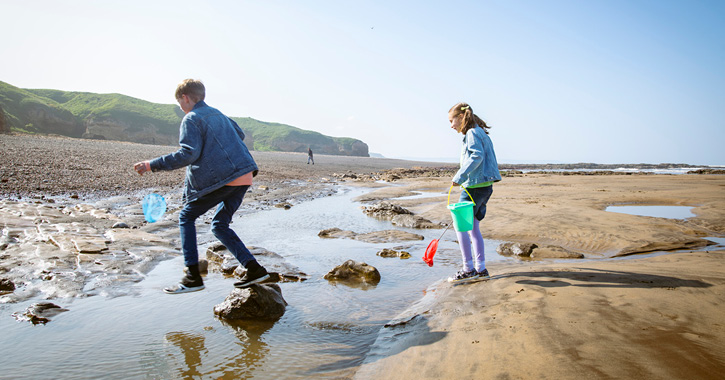 two children rock pooling and jumping on blackhall beach, Durham Heritage Coast